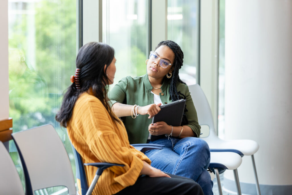 Woman in waiting room talking to a therapist holding a tablet