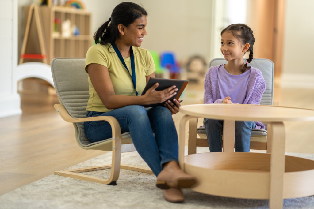 Woman therapist on an ipad sitting at a table with a young girl